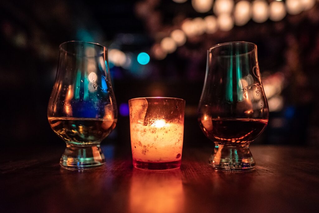 selective focus photography of two clear footed glasses placed near votive candle on table whiskeyandwhisky.com